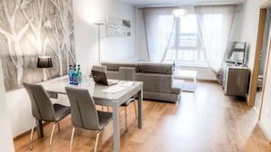 Ett modernt vardagsrum med en grå soffa, ett matbord med stolar, en platt-TV och en stor, abstrakt tavla på väggen.