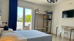 Une chambre d’hôtel équipée d’un lit, d’un bureau, d’une chaise, d’une télévision et d’un balcon donnant sur un paysage verdoyant.