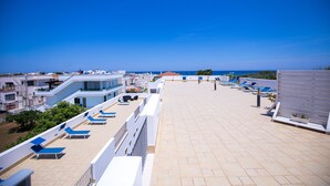 Une terrasse sur le toit avec des chaises longues, une vue sur la mer et des bâtiments modernes en arrière-plan.