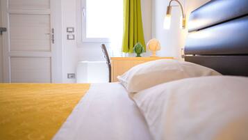 Habitación de hotel con cama, escritorio, silla, lámpara y ventana con cortinas.