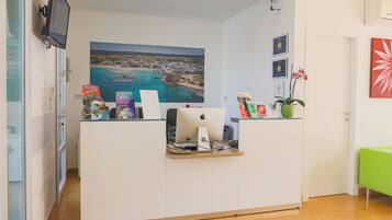 A reception desk with a computer, a large window with a view of a coastal town, and a green sofa in the corner.