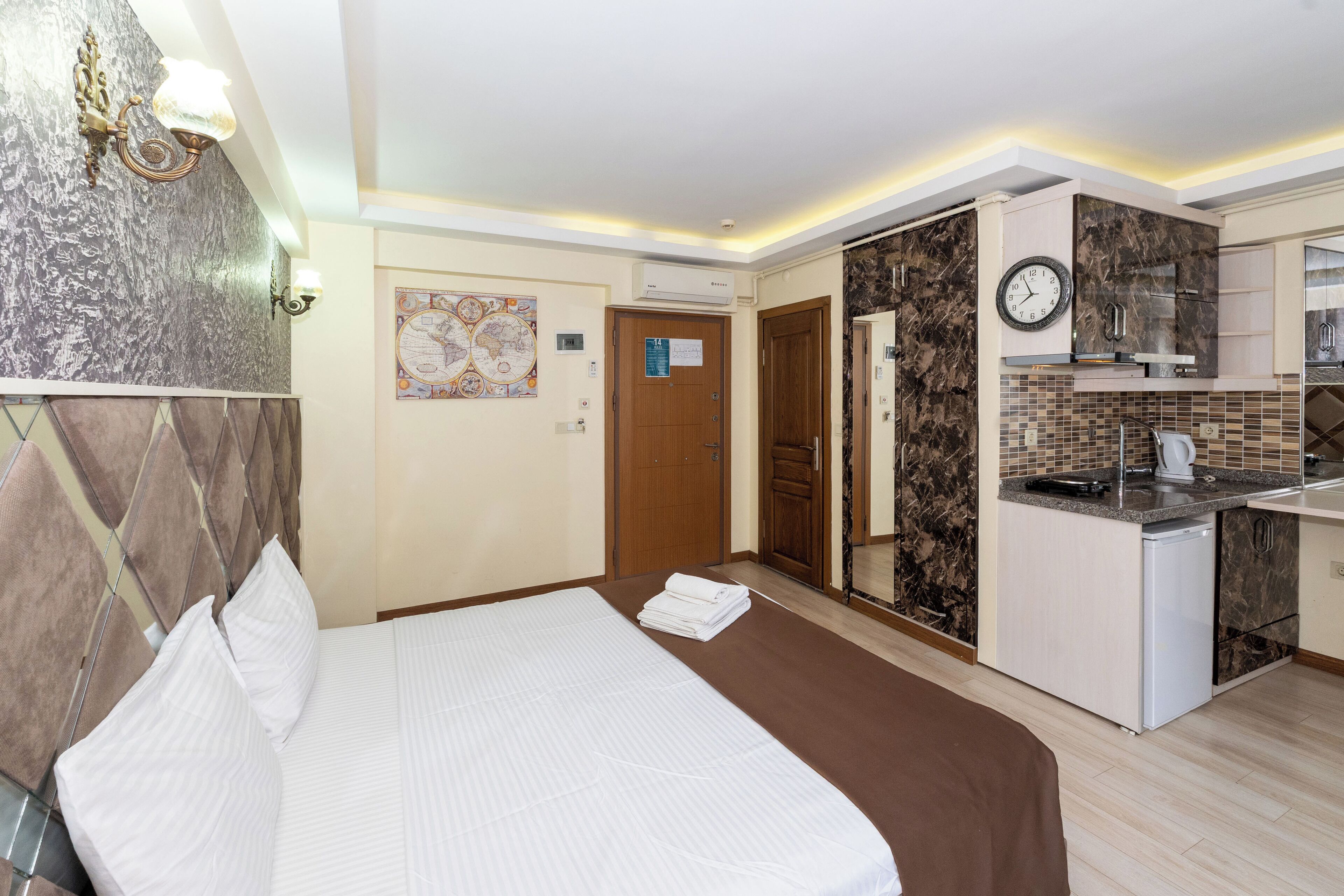 Une chambre d’hôtel avec un lit, une petite kitchenette, une porte en bois et une horloge fixée au mur.