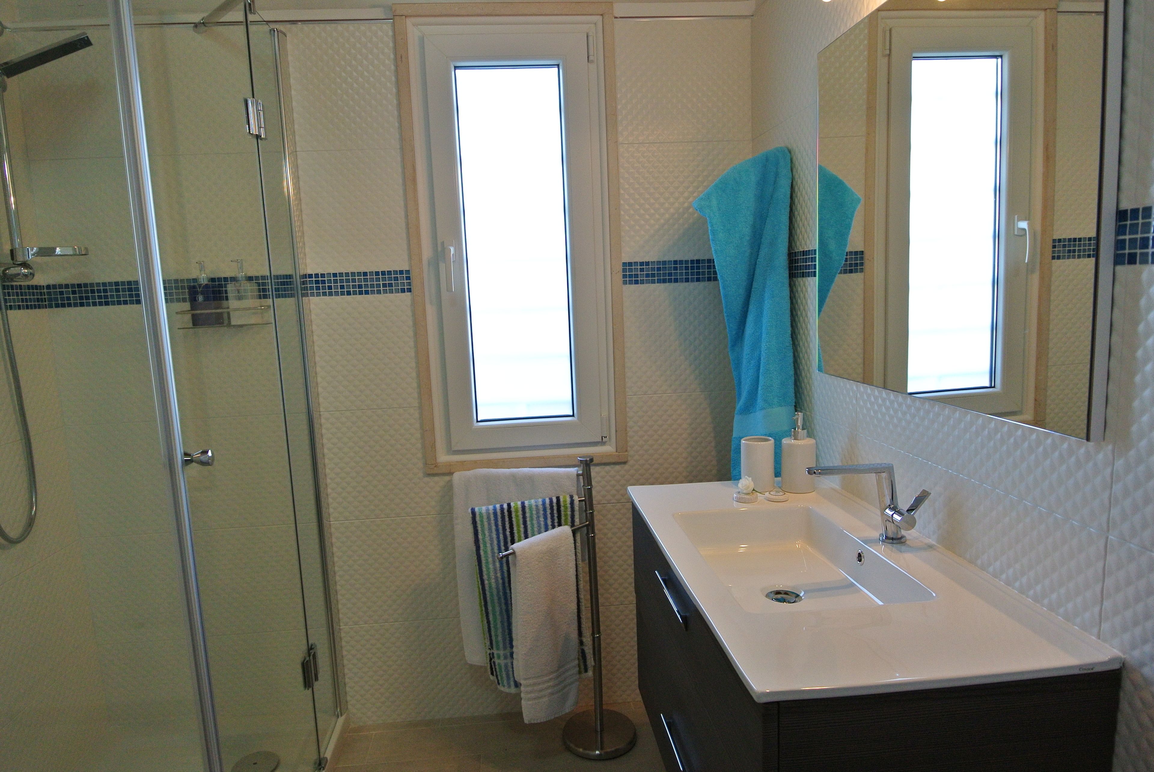 A bathroom with a glass shower enclosure, a sink with a mirror, and a window with a view.