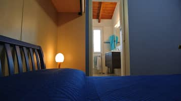 Un dormitorio con cama, mesita de noche, lámpara y vistas a un baño con toallero y espejo.