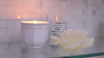 Una vela blanca y un frasco de colonia Monotheme White Musk sobre una superficie de vidrio.