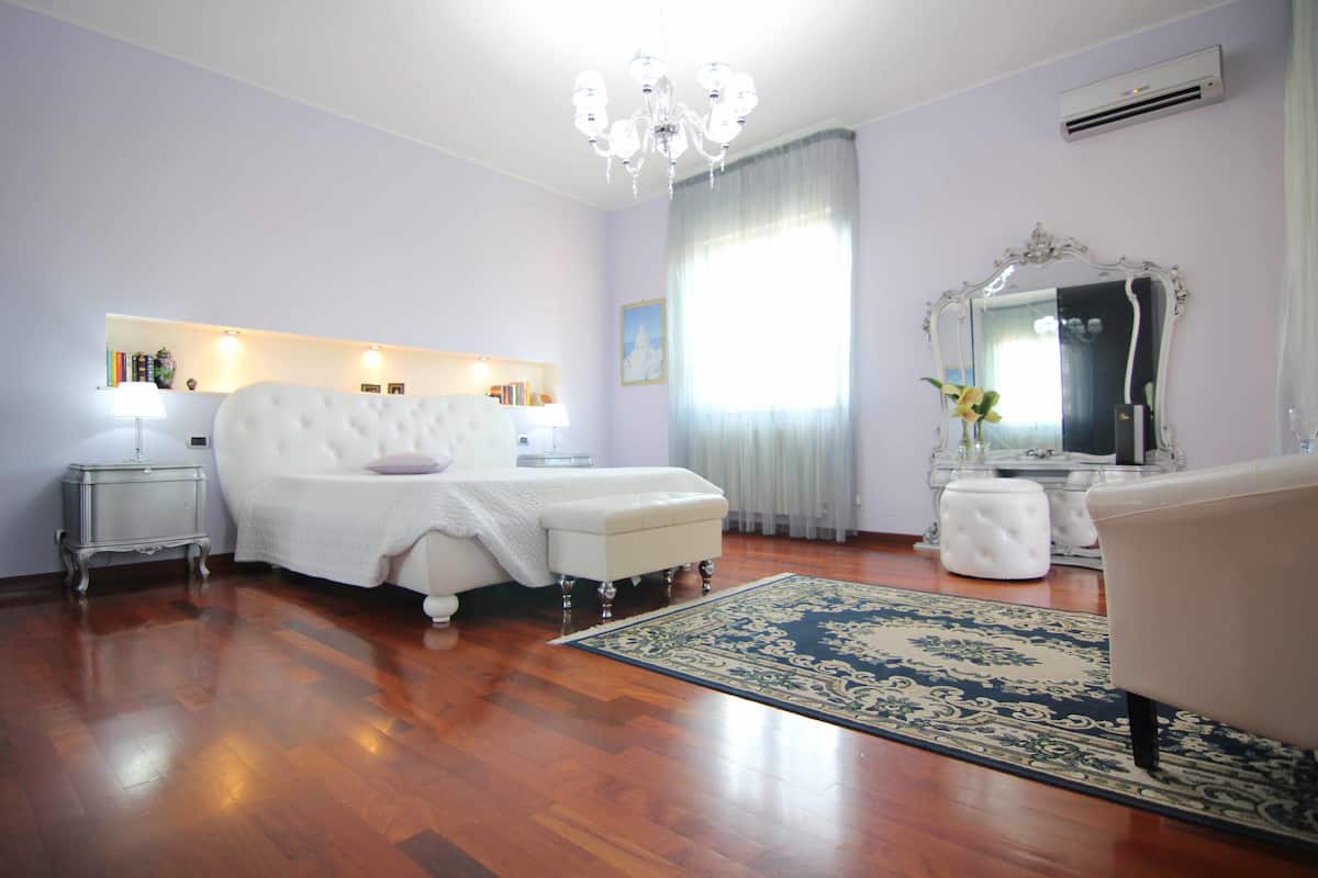 Un dormitorio con una cama grande, un tocador con espejo, una araña y suelo de madera.