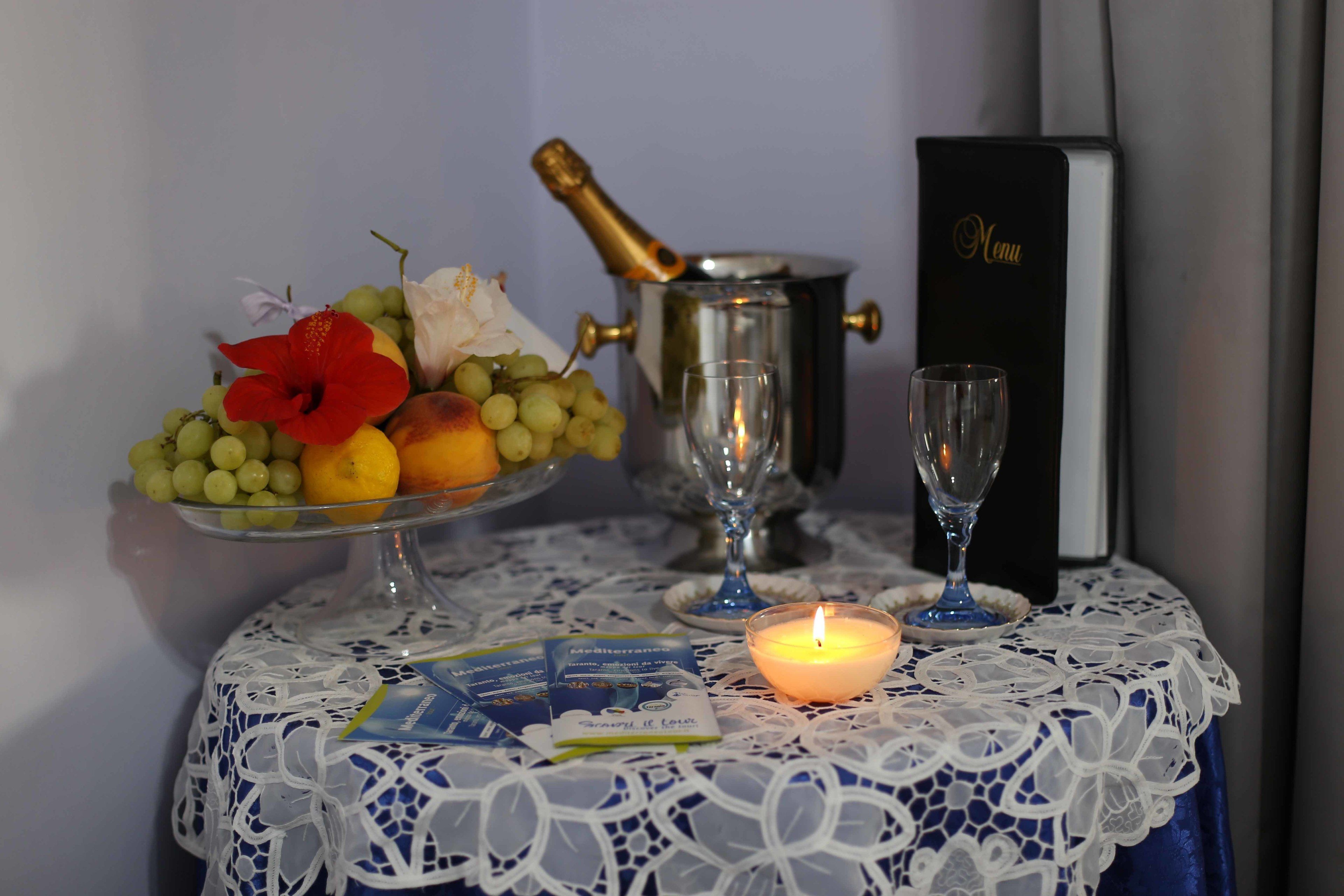 A table with a fruit bowl, a candle, a menu, and a champagne bottle.