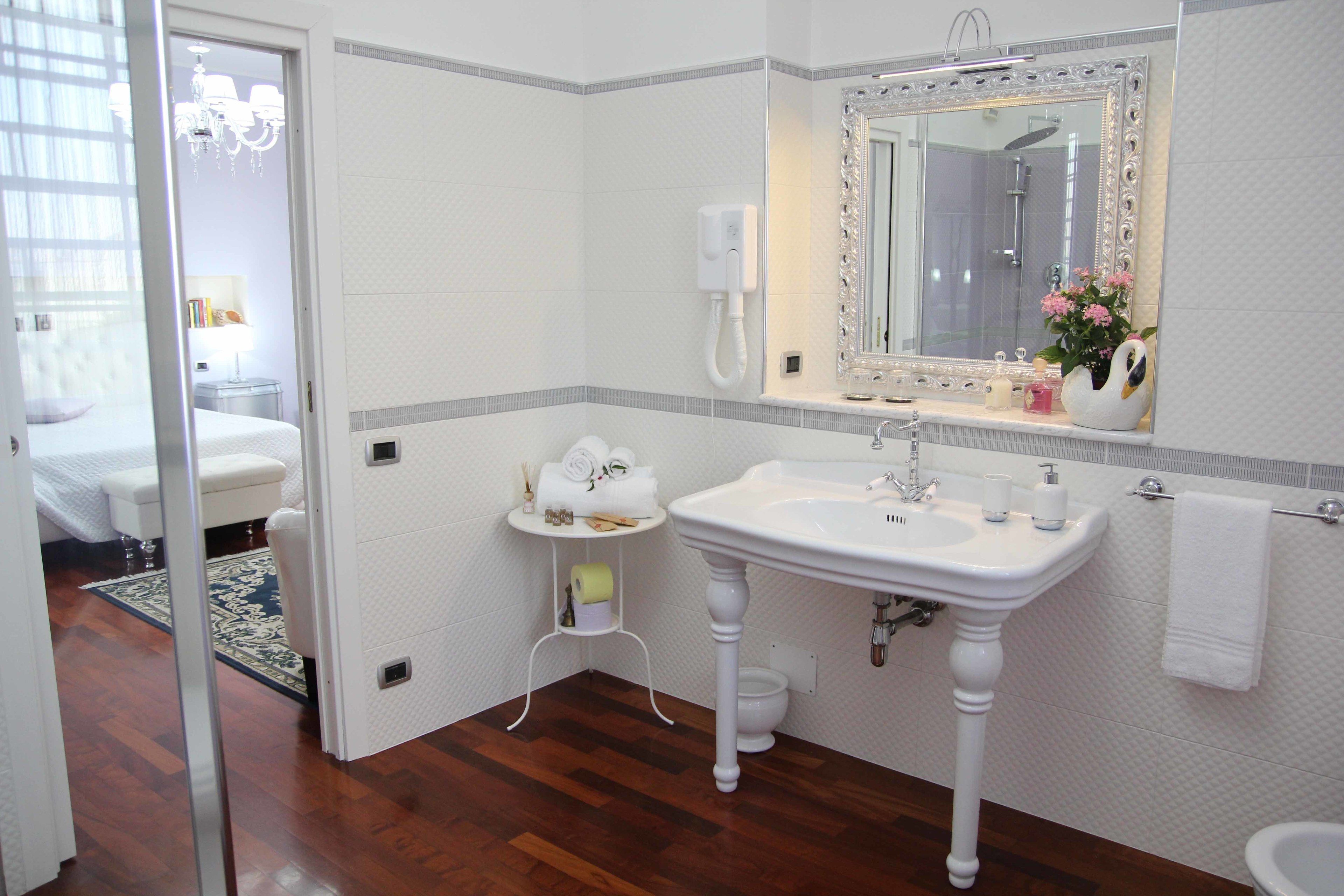 Une salle de bain avec un lavabo blanc, un miroir et des toilettes. On y trouve une petite table avec des articles de toilette et un porte-serviettes.