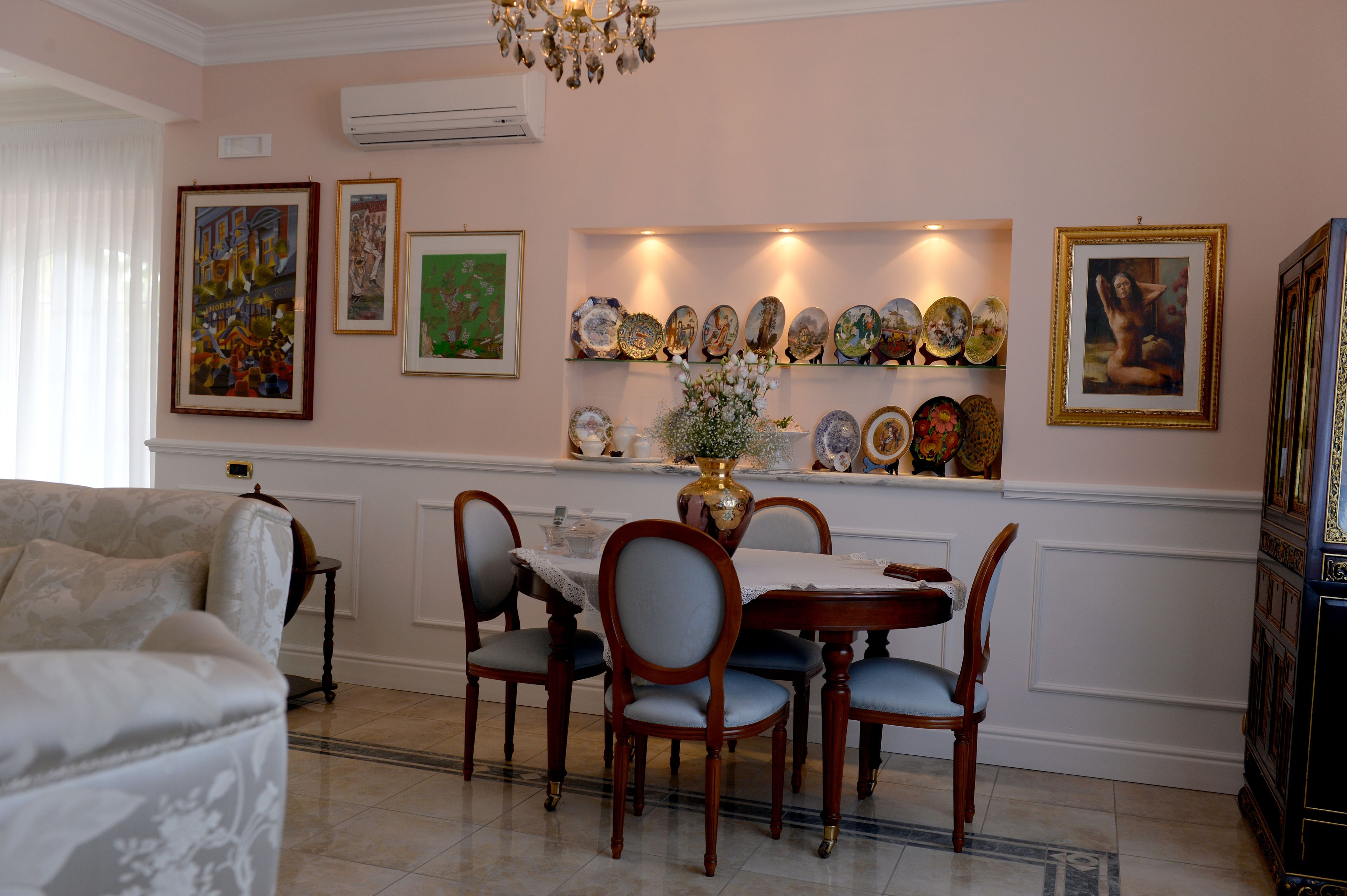 A dining area with a table set for four, surrounded by chairs, and a wall decorated with framed artwork and plates.
