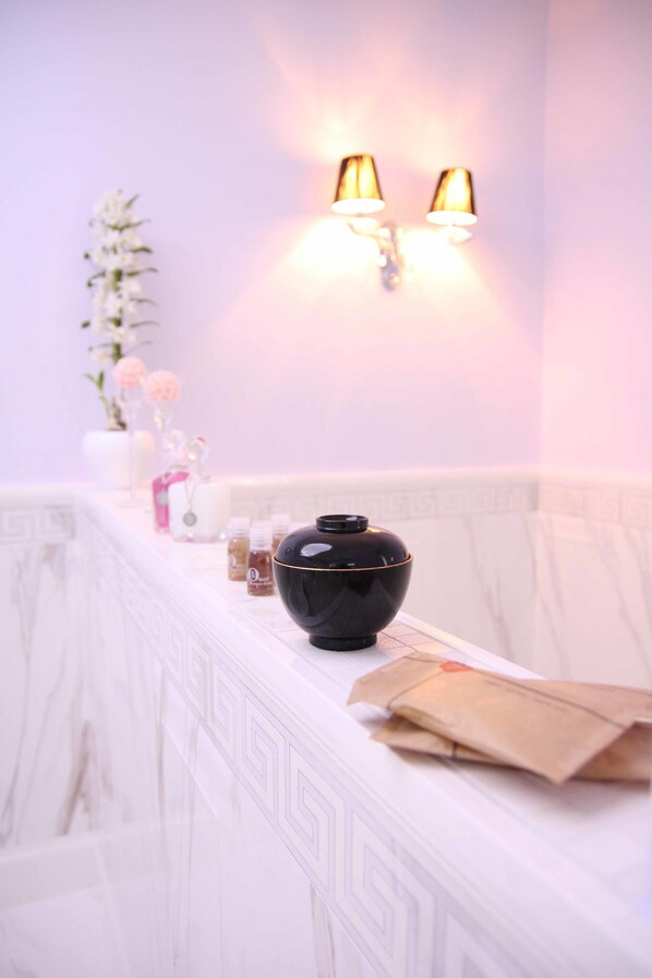 A bathroom with a white marble countertop, a black vase, and a wall-mounted light fixture.