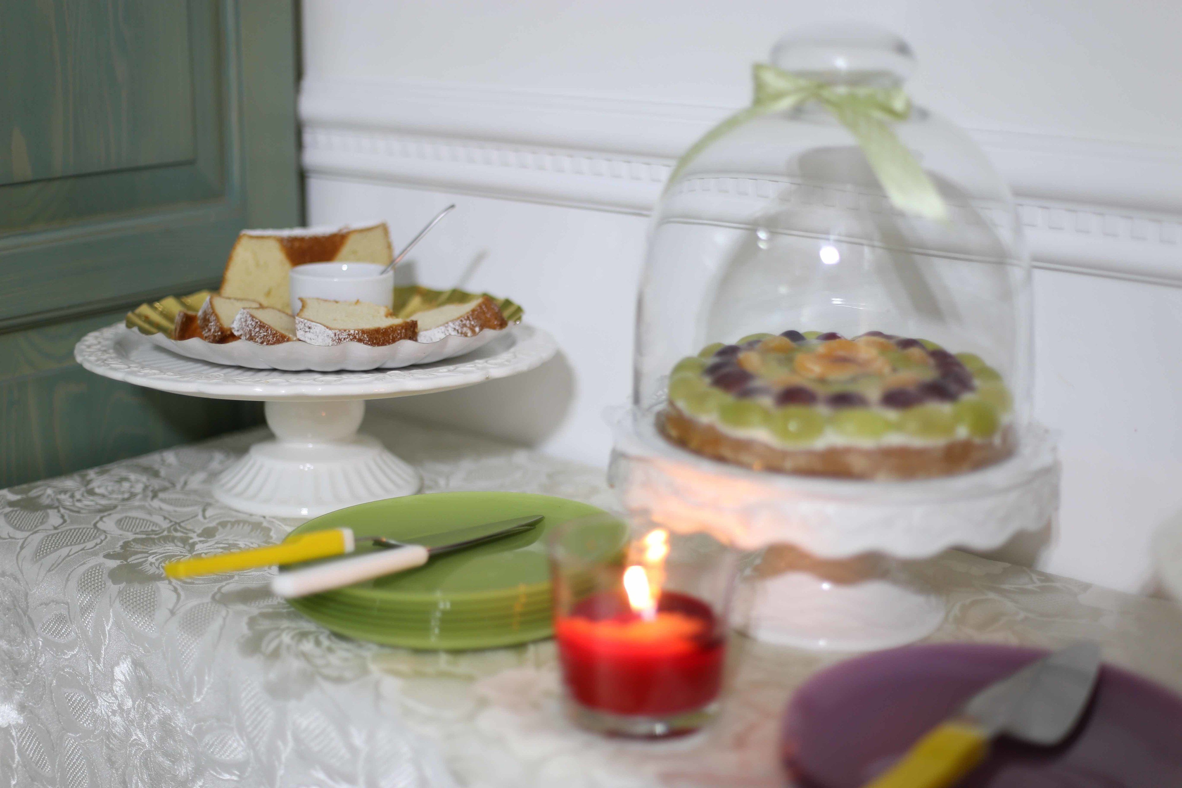 A table with a cake on a stand, a candle, and a knife.