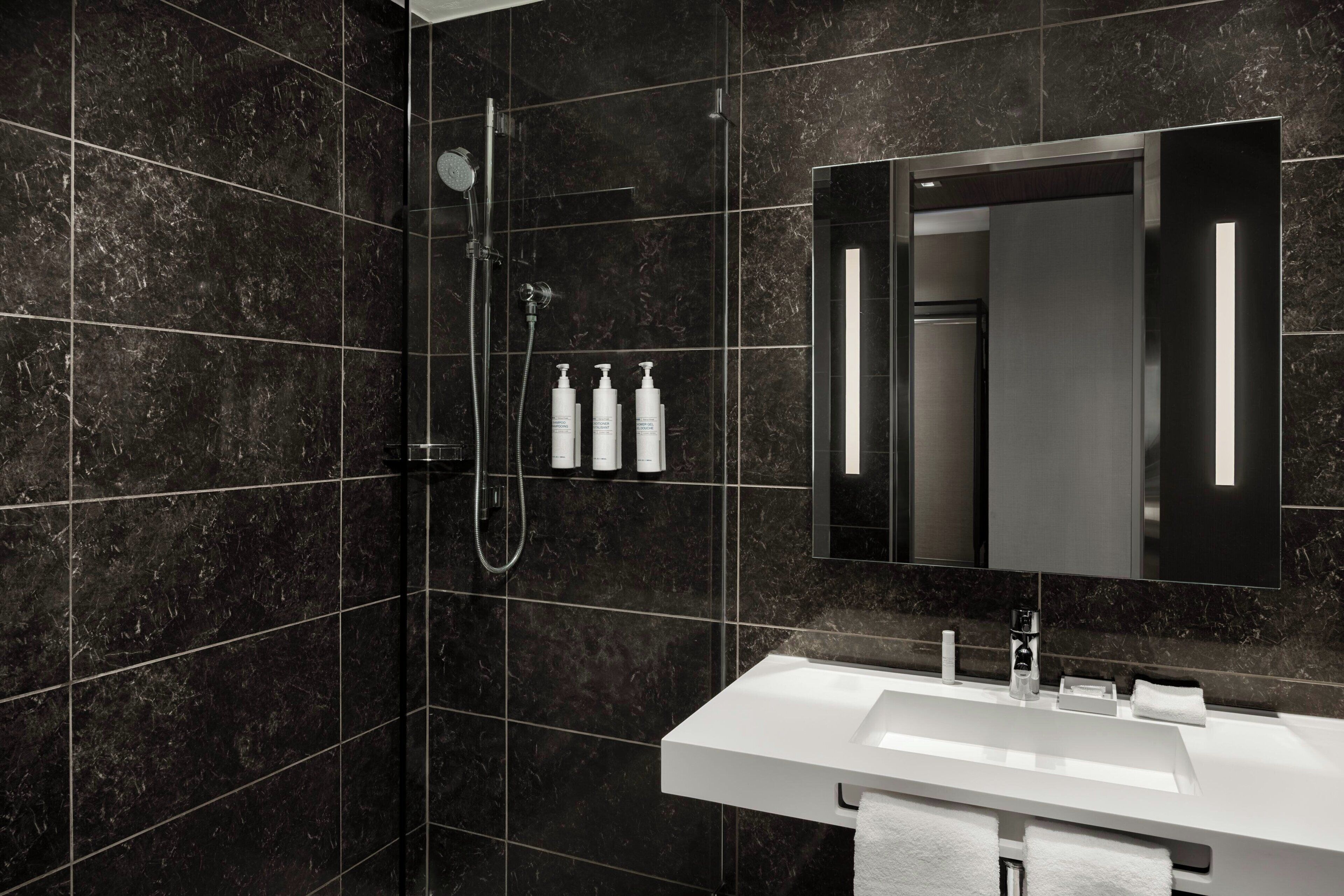 A modern bathroom with a dark marble wall, a white sink, and a large mirror.