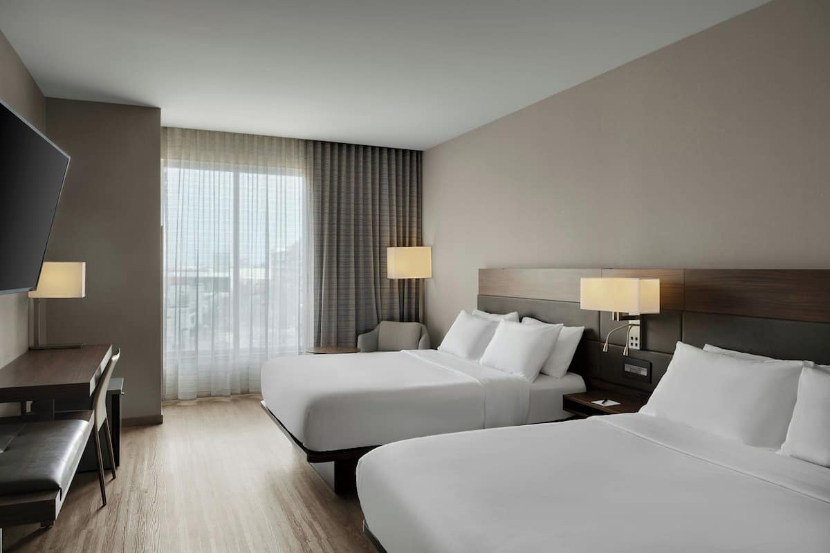Ein Hotelzimmer mit zwei Betten, einem Schreibtisch und einem Fernseher.