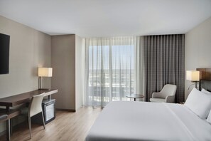 A hotel room with a bed, desk, chair, and a small table. - AC Hotel by Marriott Cincinnati at Liberty Center (West Chester)