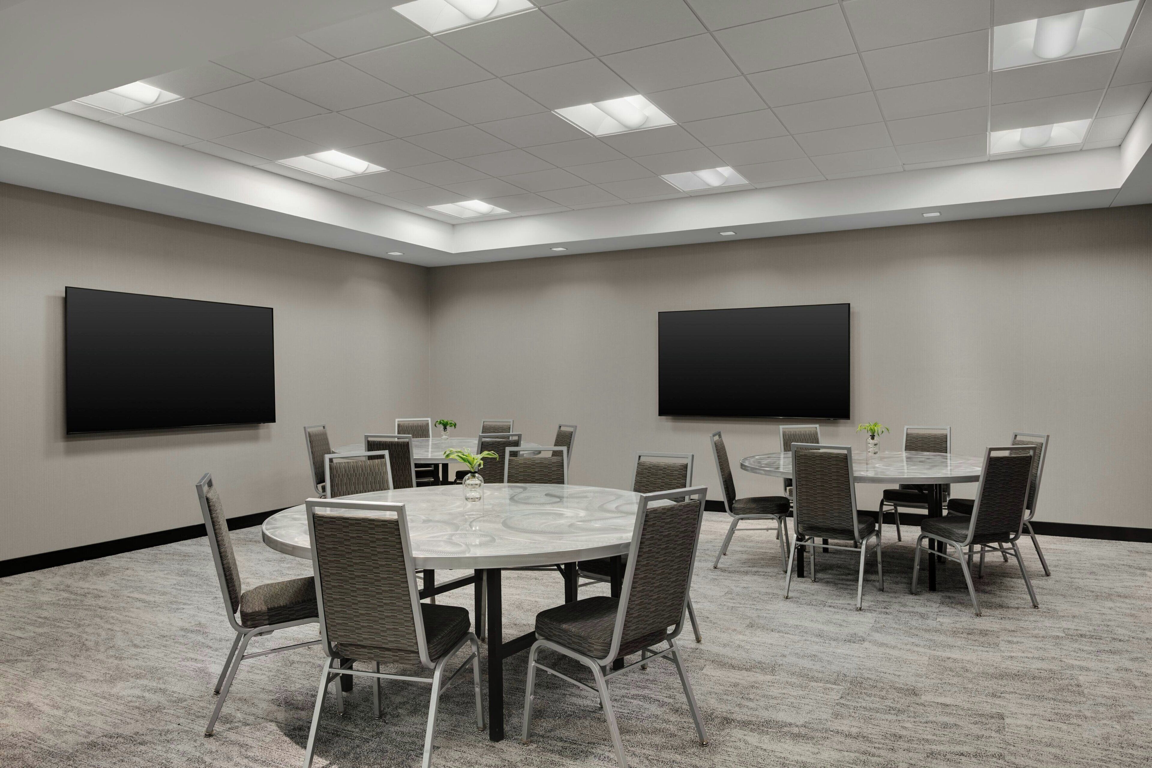 A conference room with a round table, chairs, a flat-screen TV, and a carpeted floor.