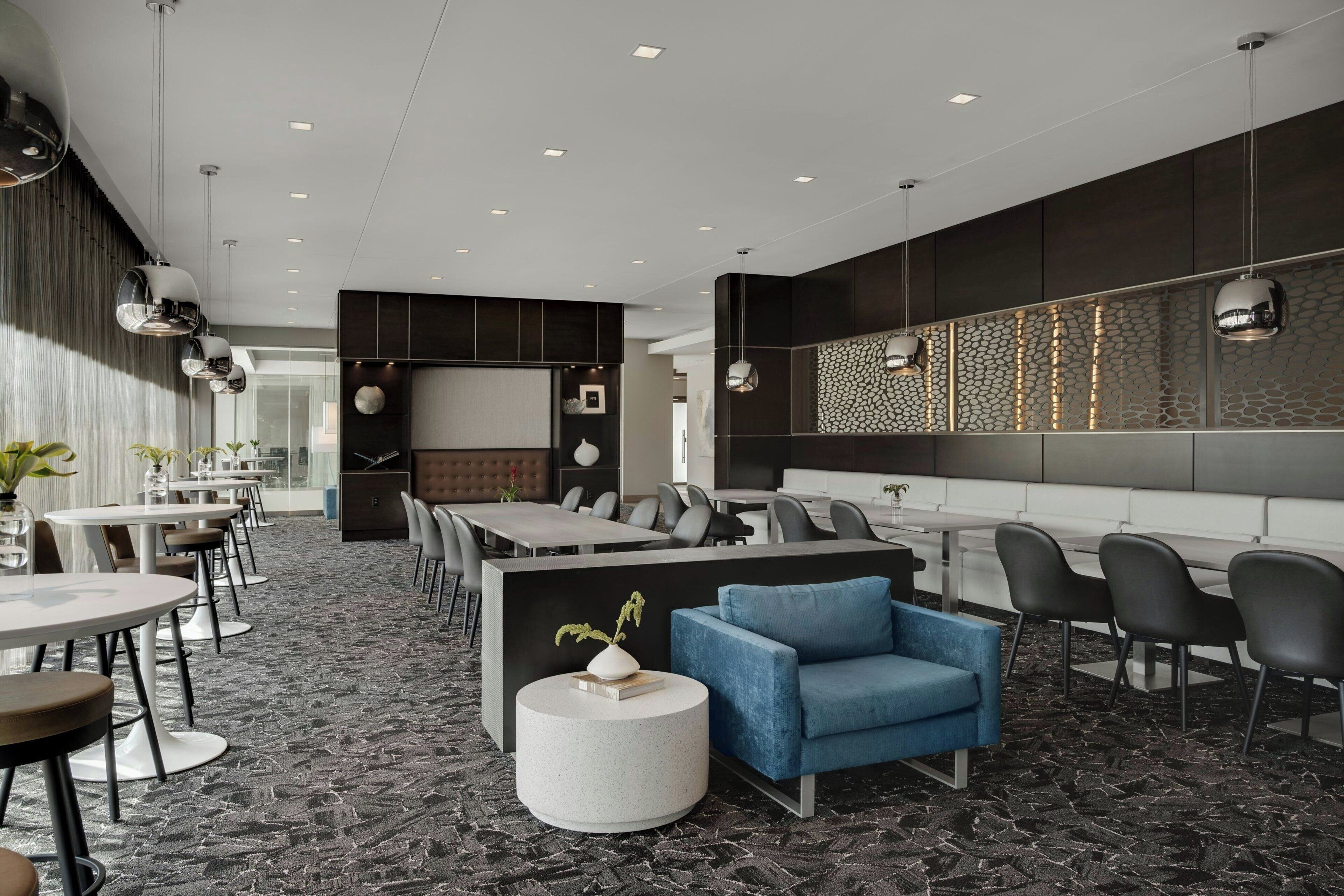 A modern hotel lobby with a mix of seating areas, including round tables and sofas, a reception desk, and a decorative wall with a textured pattern.