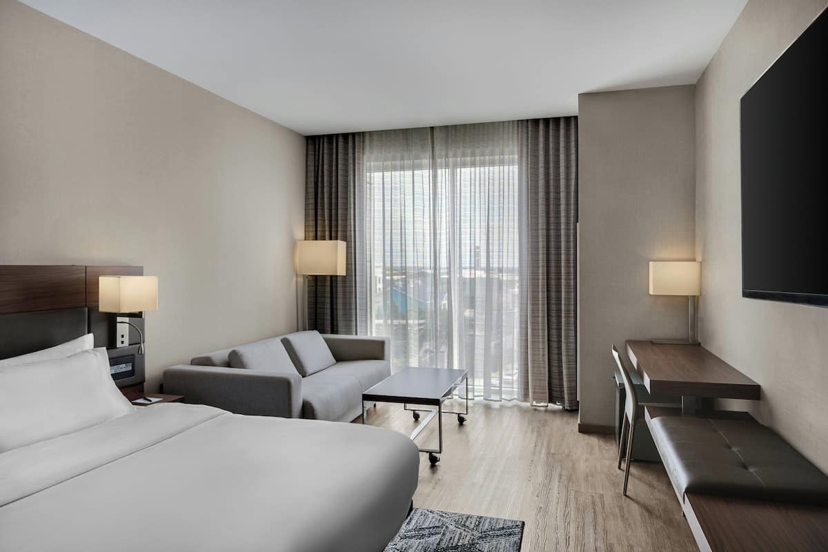 Ein modernes Hotelzimmer mit einem großen Bett, einer Couch, einem Schreibtisch und einem Fernseher.