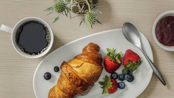A croissant on a plate with strawberries and blueberries, a cup of coffee, and a spoon.