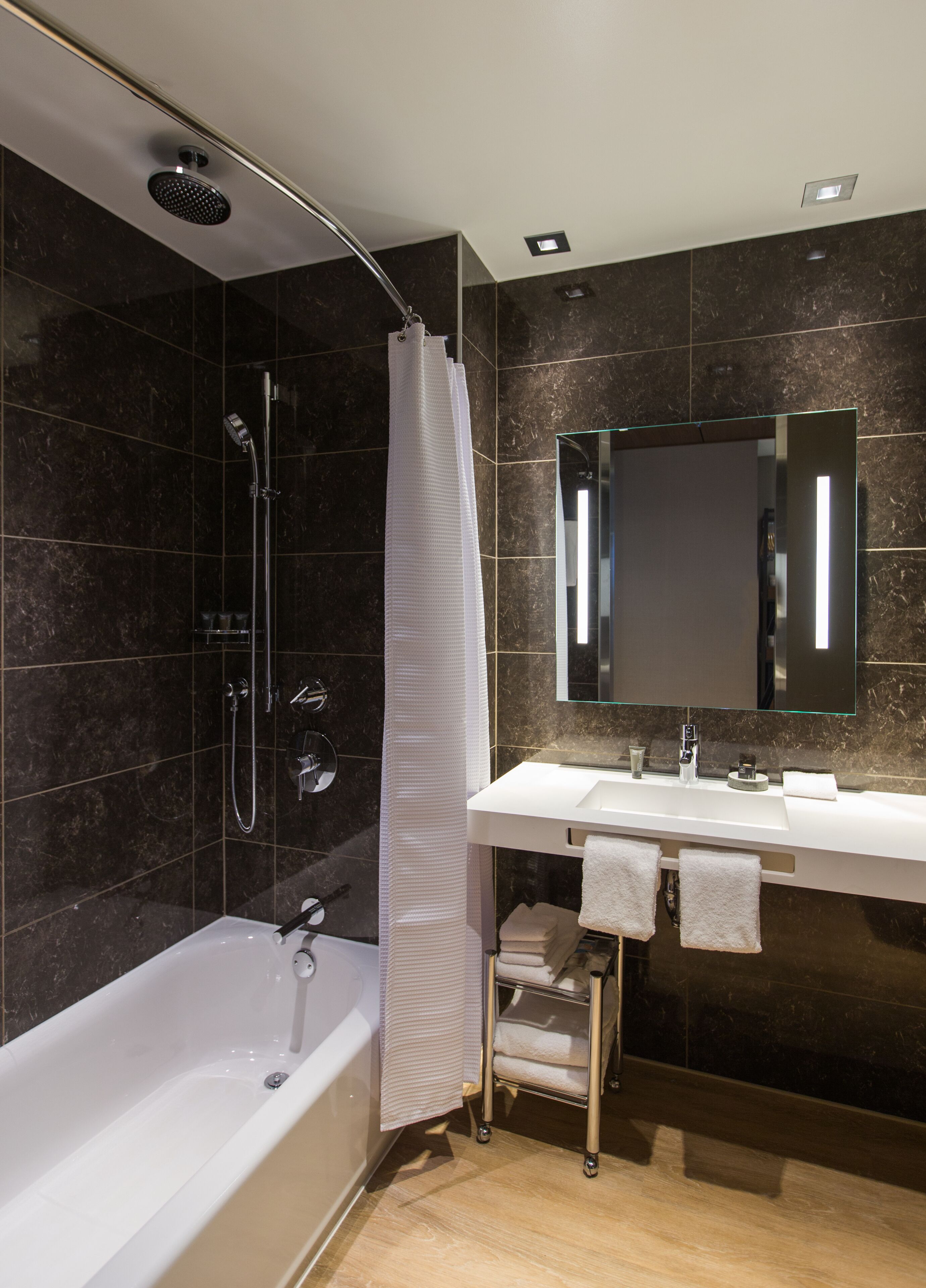 A modern bathroom with a bathtub, a shower, a vanity with a mirror, and a towel rack.