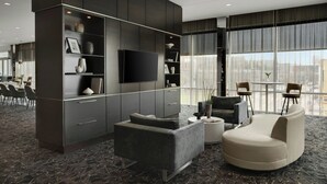 Un moderno vestíbulo de hotel con un televisor de pantalla plana grande, paneles de madera oscura, una zona de estar con sofá y sillones, y un ventanal con vistas a la ciudad.