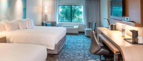 A hotel room with a large bed, a desk with a chair, a TV, and a window with a view of palm trees.