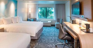 Habitación de hotel con una cama grande, un escritorio con silla, televisión y ventana con vistas a palmeras.