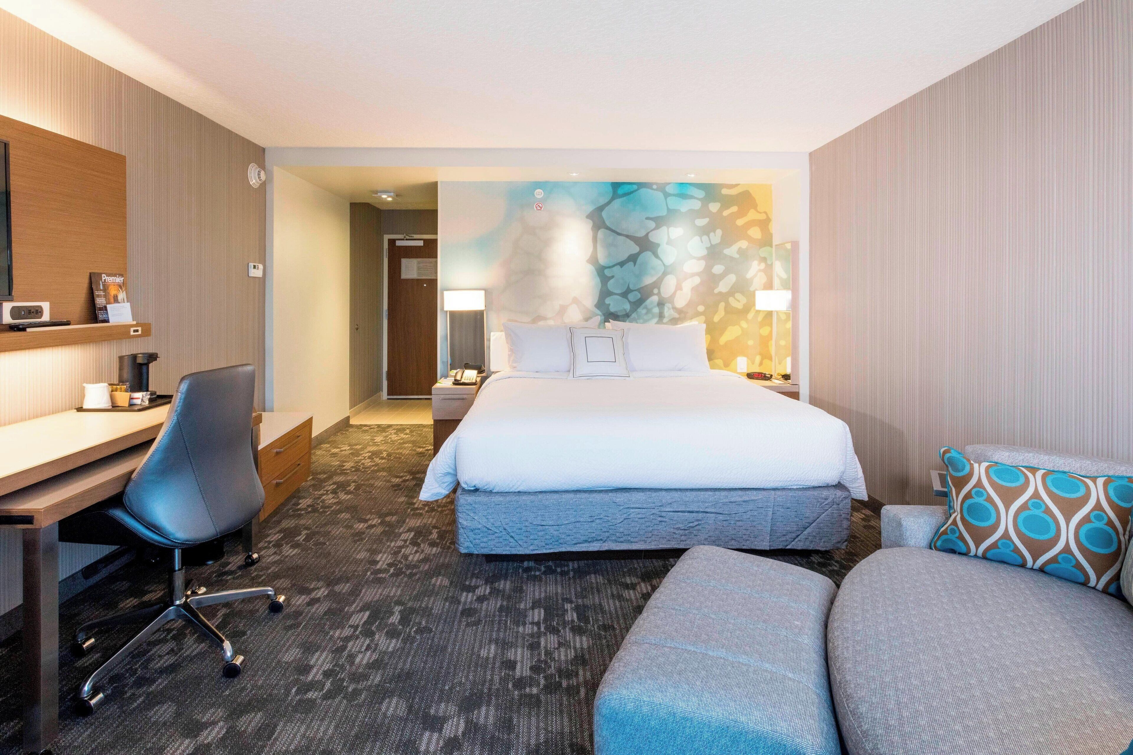 A hotel room with a bed, a desk, a chair, a sofa, and a wall with a textured design.