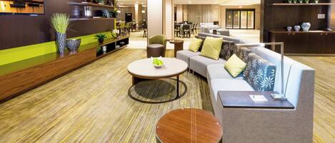 En modern hotellobby med en soffa, runda bord och en receptionsdisk.