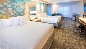 A hotel room with two beds, a desk, a chair, a TV, and a large window with curtains.