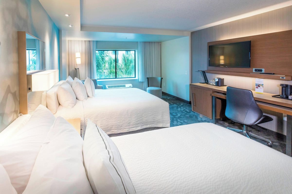 Een hotelkamer met twee bedden, een bureau met stoel, een televisie en een raam met gordijnen.