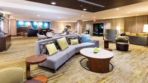 A hotel lobby with a sectional sofa, armchairs, a round coffee table, and a reception desk.