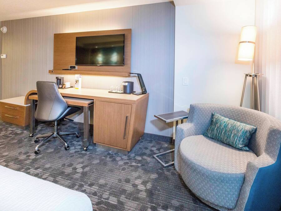 A hotel room with a bed, a desk with a chair, a television, and a lamp.