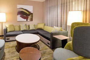 Una habitación de hotel moderna con sofá modular, dos mesas redondas de centro y un sillón individual.