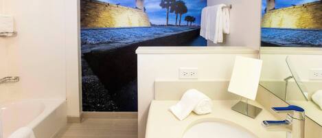A modern bathroom with a bathtub, a sink with a mirror, and a wall mural depicting a coastal scene.