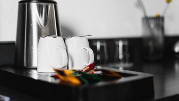 A stainless steel coffee maker and two white mugs on a tray.