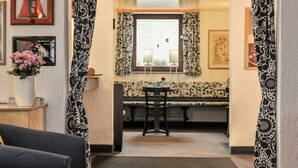 A room with a dining table, chairs, a radiator, a window with patterned curtains, and a framed picture on the wall. - City Hotel Fellbach (Fellbach)
