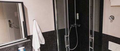A modern bathroom with a glass-enclosed shower, a white sink, and a toilet.