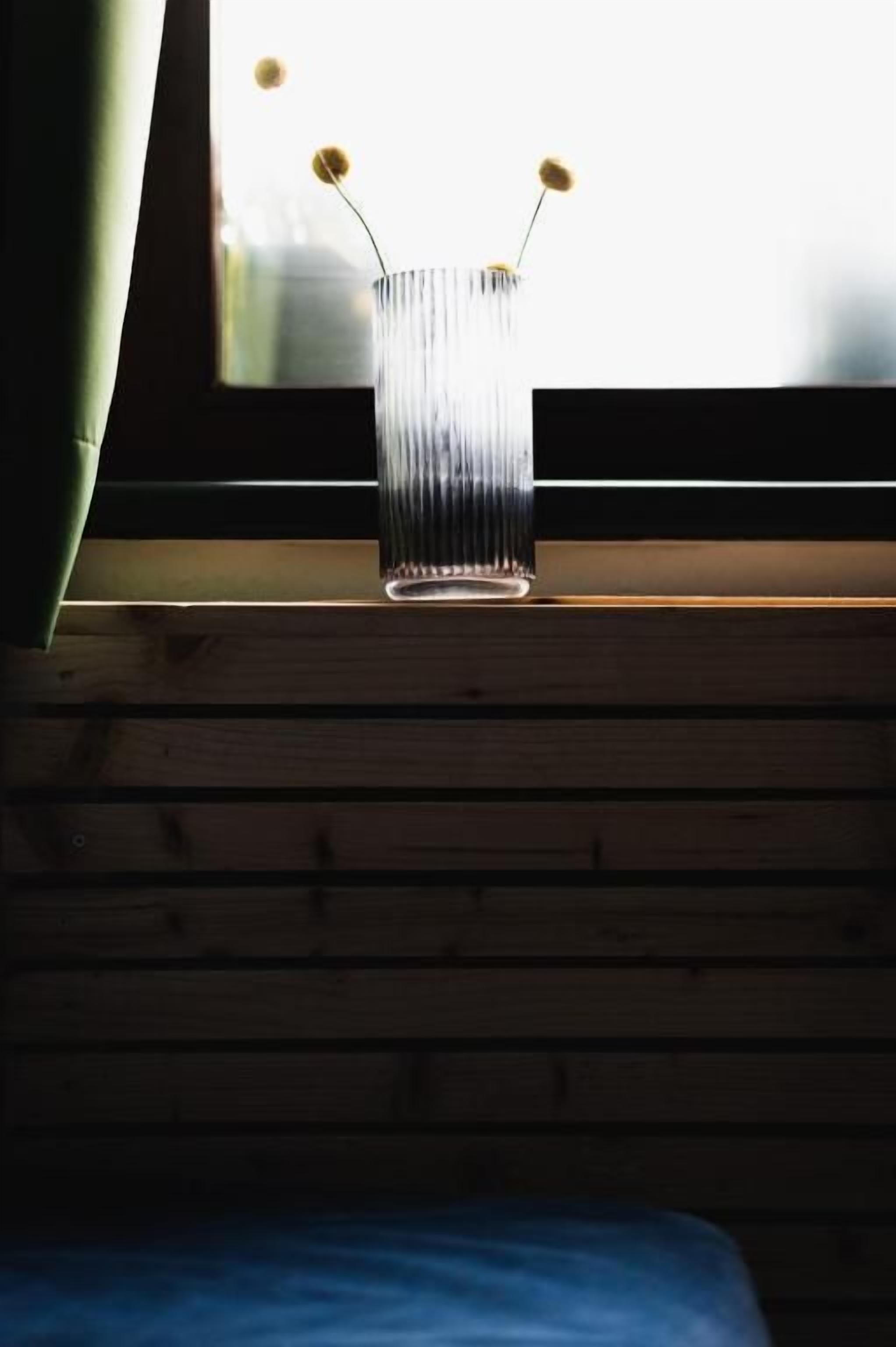 A clear glass vase with a ribbed texture on a wooden ledge by a window.