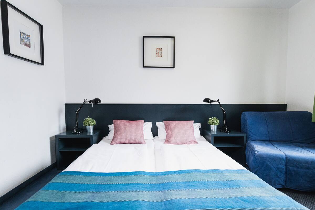 A hotel room with a large bed, two bedside tables with lamps, a blue chair, and a framed picture on the wall.