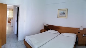 A hotel room with two beds, a wooden headboard, bedside lamps, a small bedside table, and a framed picture on the wall. - Solemar Apartments (Rhodes)