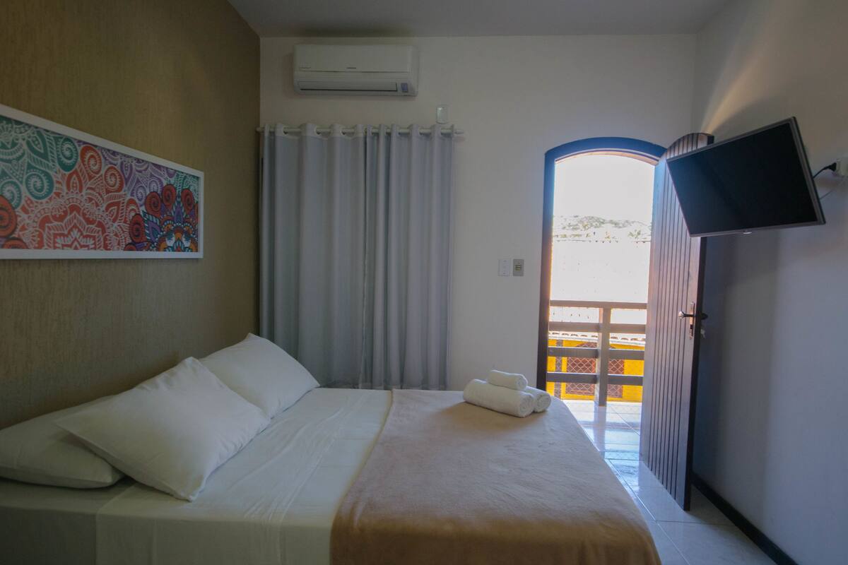 A hotel room with a bed, a TV, a painting, and a view of the outside.