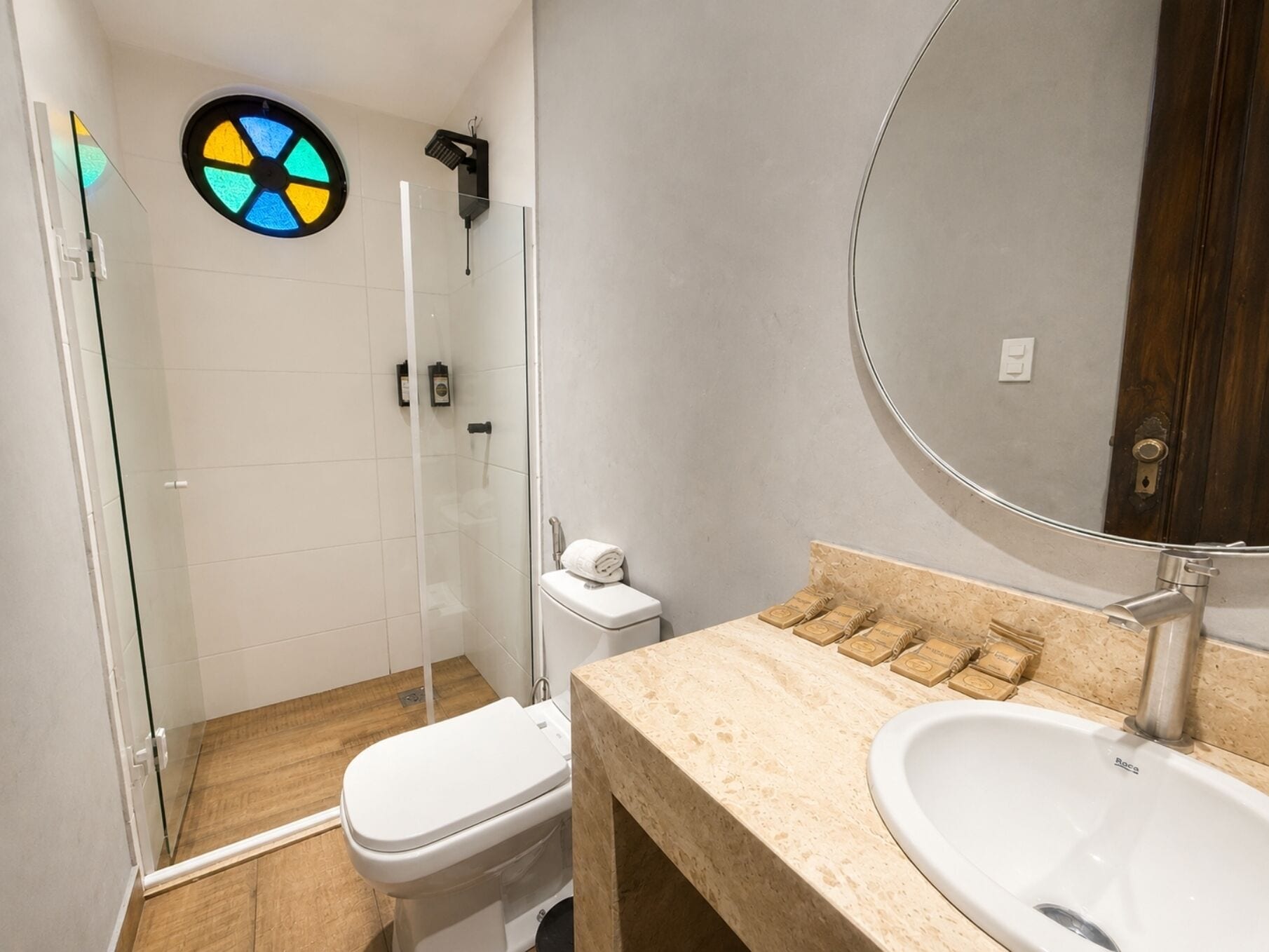 A bathroom with a glass shower enclosure, a toilet, a sink with soap dispensers, and a mirror.