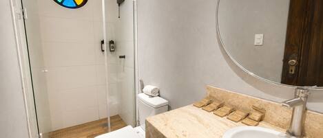 A bathroom with a glass shower enclosure, a toilet, a sink with soap dispensers, and a mirror.