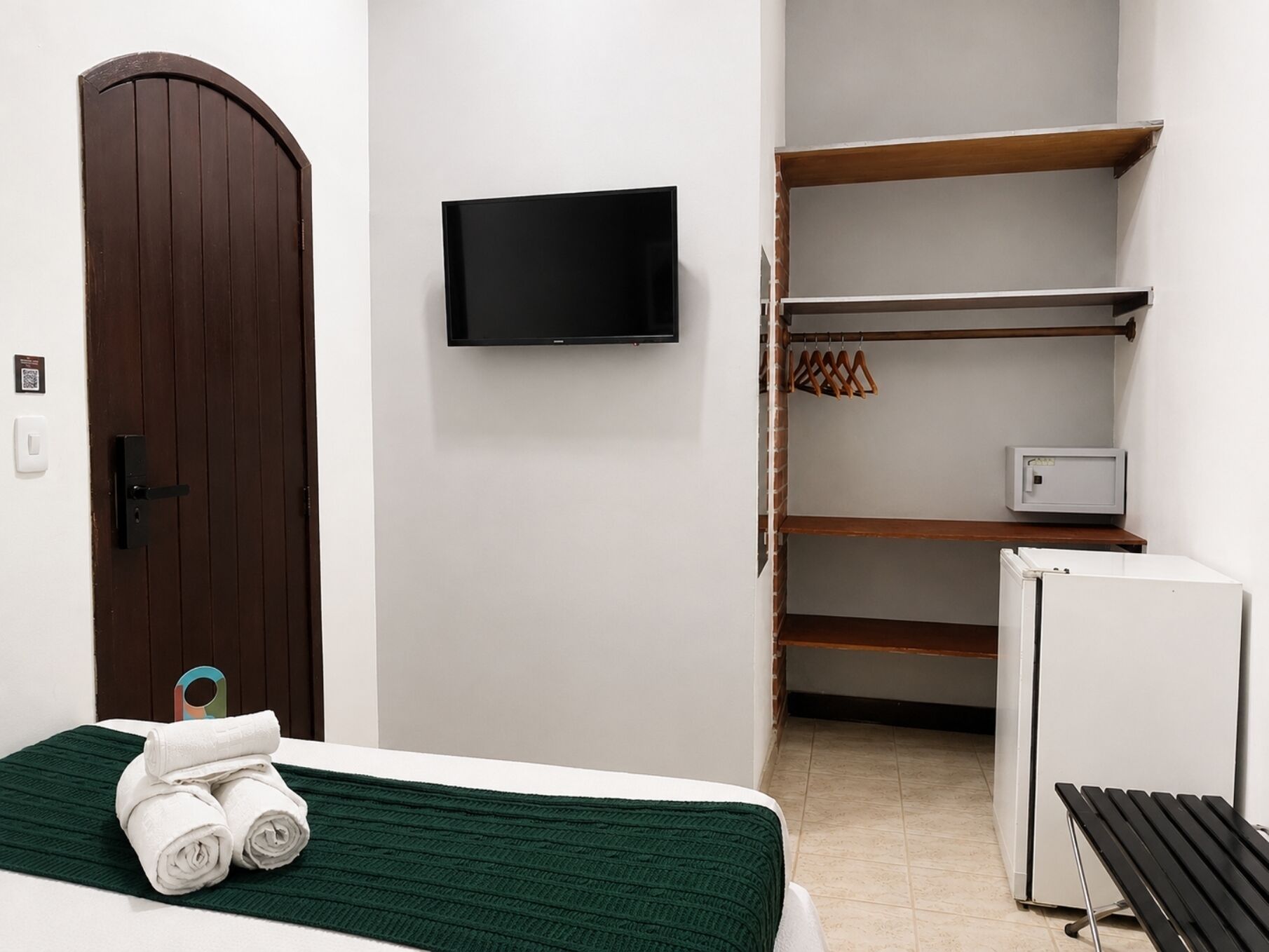 A hotel room with a bed, a television, a wardrobe, and a small refrigerator.
