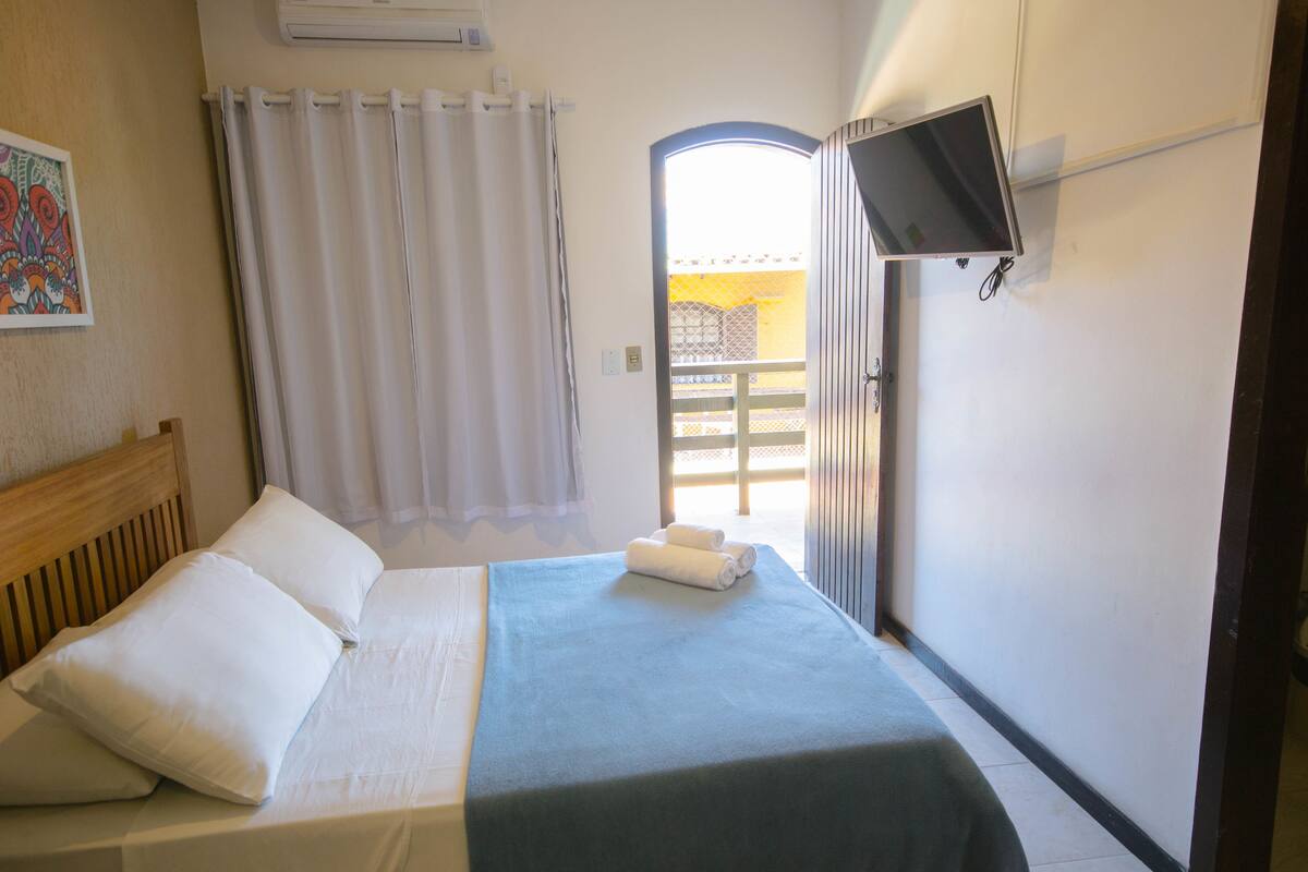 A hotel room with a bed, a TV mounted on the wall, and a view of the outside balcony.