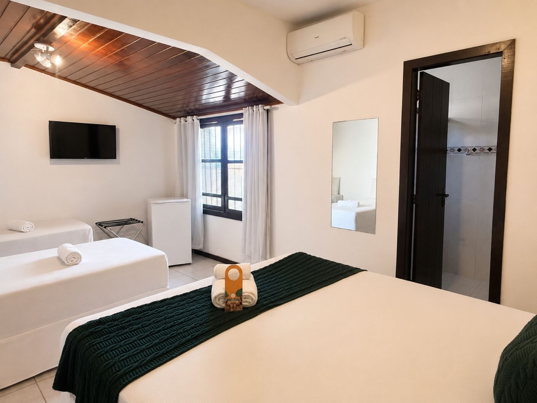 A hotel room with a bed, a seating area with a chair and a small table, a television mounted on the wall, and a window with curtains.