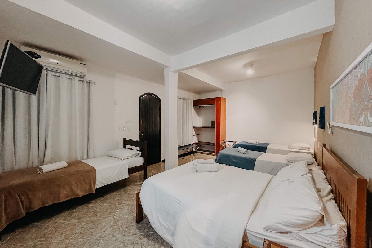A hotel room with two single beds, a large bed, a TV mounted on the wall, a wardrobe, and a mirror.