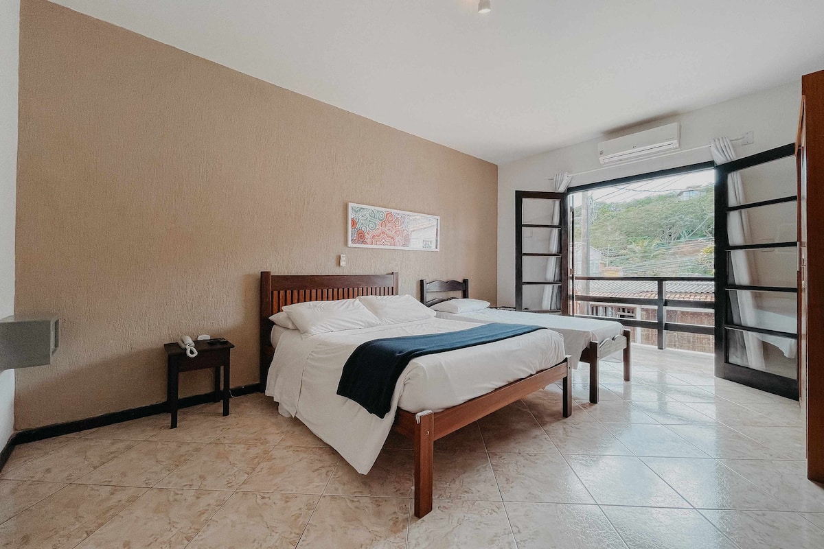 A bedroom with a bed, a nightstand, a window with curtains, and a wall-mounted air conditioner.