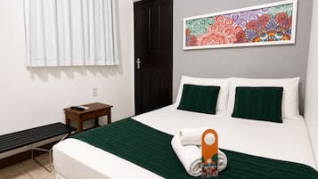 A hotel room with a bed, a small table, a bench, a door, and a colorful artwork on the wall.