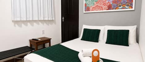 A hotel room with a bed, a small table, a bench, a door, and a colorful artwork on the wall.